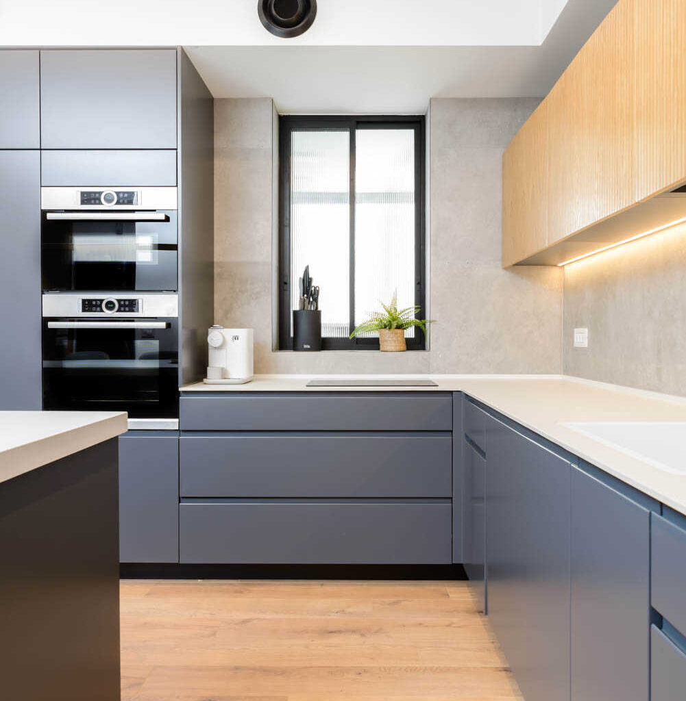 Modern kitchen with gray cabinets, wood accents, and built-in ovens.