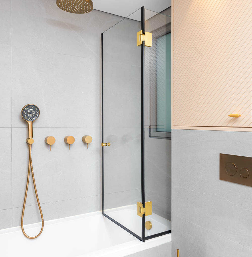 Modern bathroom with gold fixtures, white bathtub, and glass shower screen