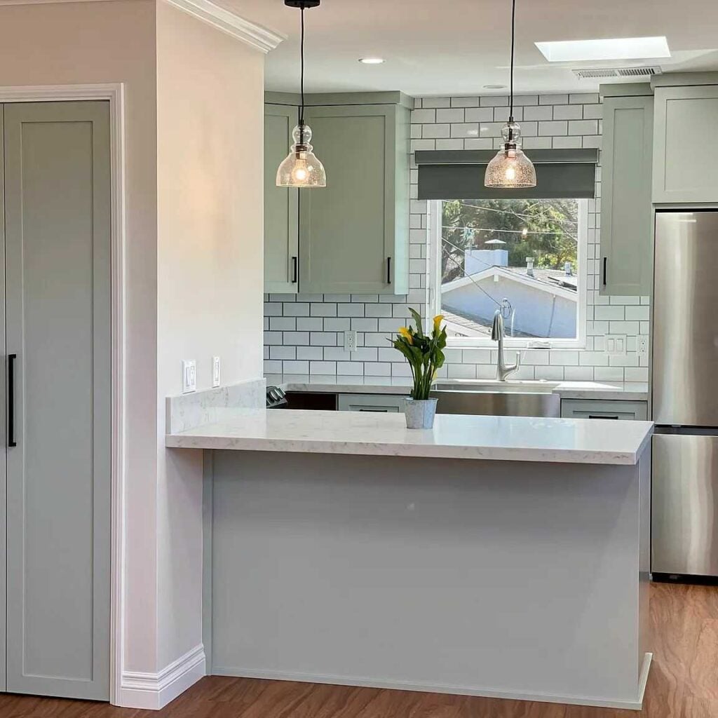 Modern kitchen with light green cabinets, white subway tile, and stainless steel appliances.