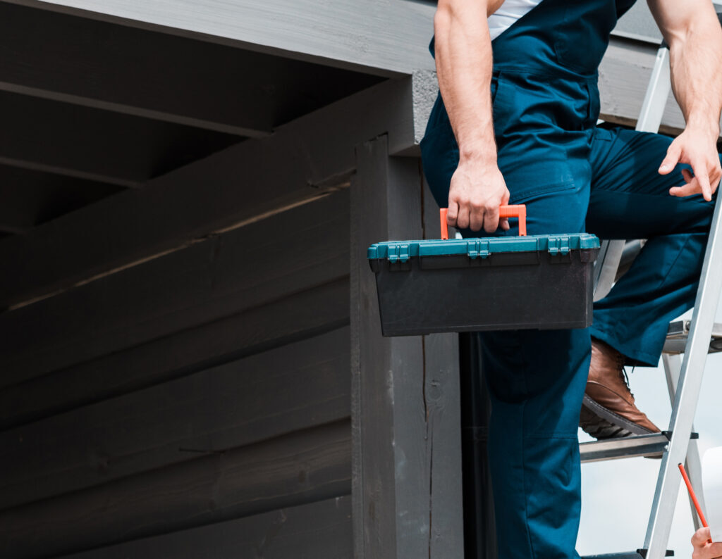 Two men working on a roof, one on a ladder, one holding plans.