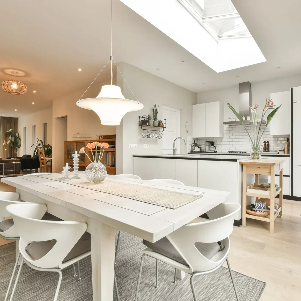Modern dining room with white table and chairs, open to a bright kitchen.