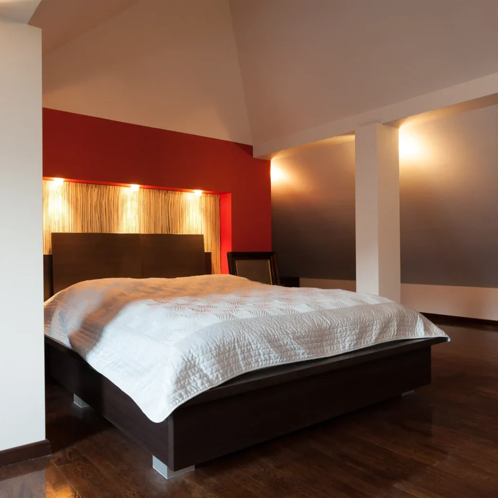 Modern bedroom with a large bed, red wall, and dark furniture.
