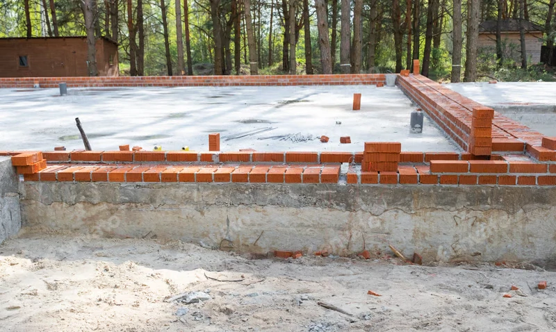 Concrete foundation with brickwork in progress surrounded by trees.