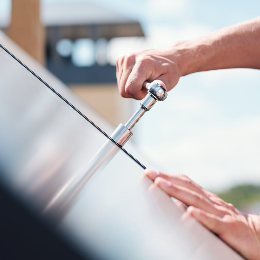 Close-up of hands tightening a bolt on a solar panel with a wrench.