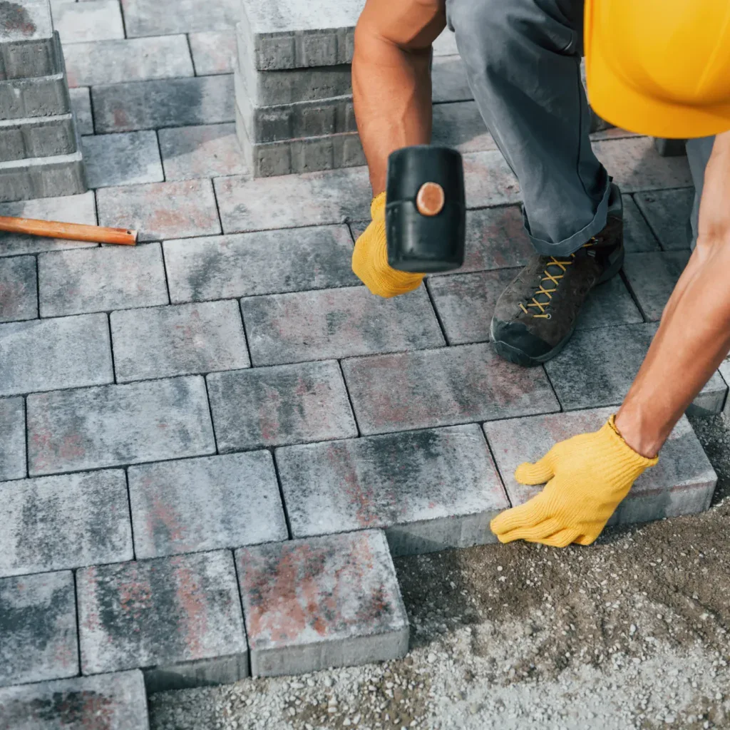 Man in yellow hard hat and gloves laying gray paving stones