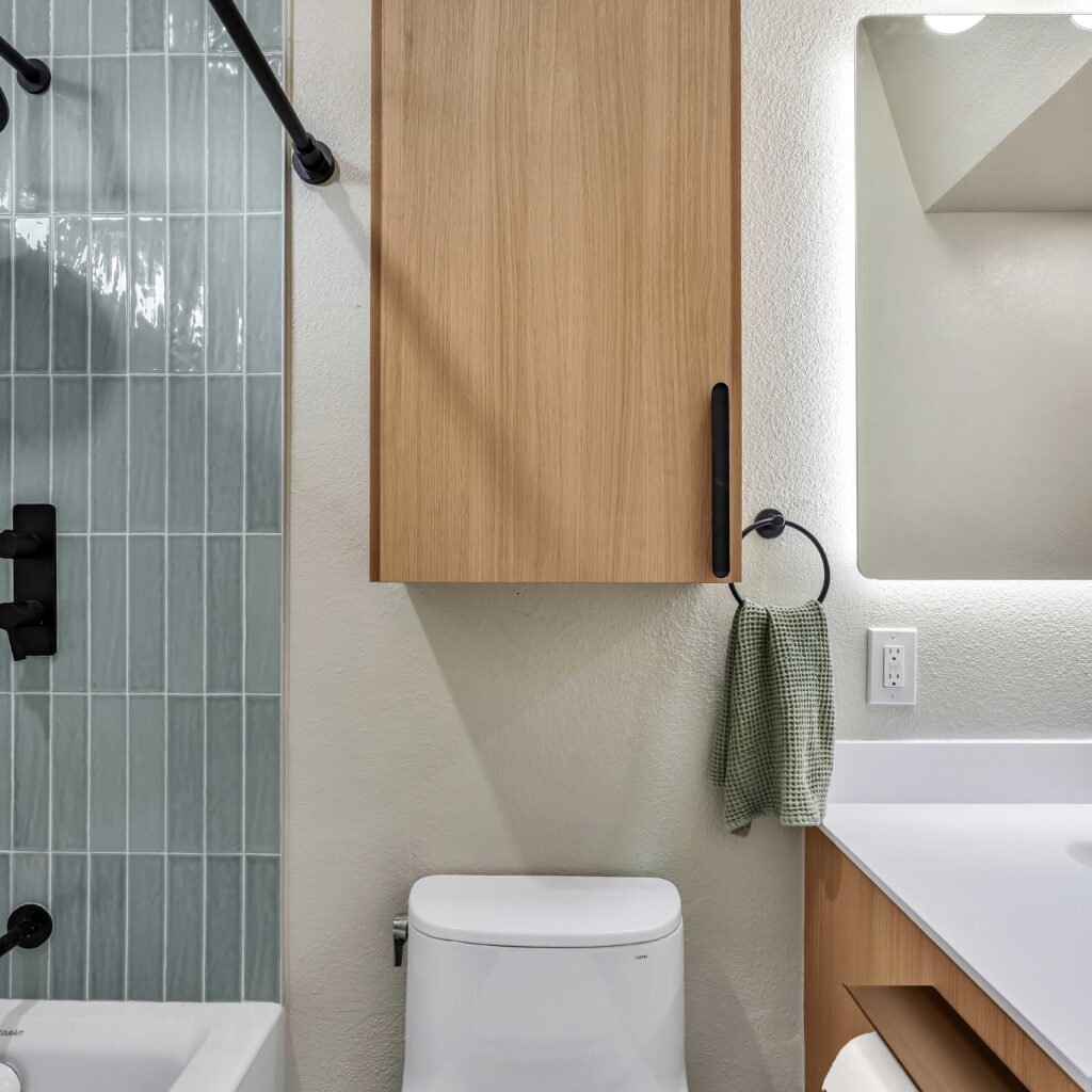 Modern bathroom with light wood cabinet, white toilet, and blue tiled shower.