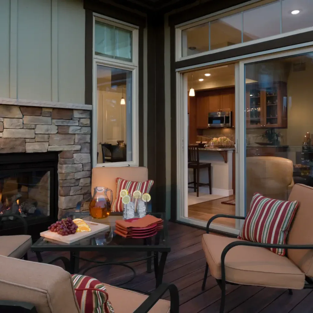 Outdoor patio with a stone fireplace, seating, and a view into a modern kitchen.