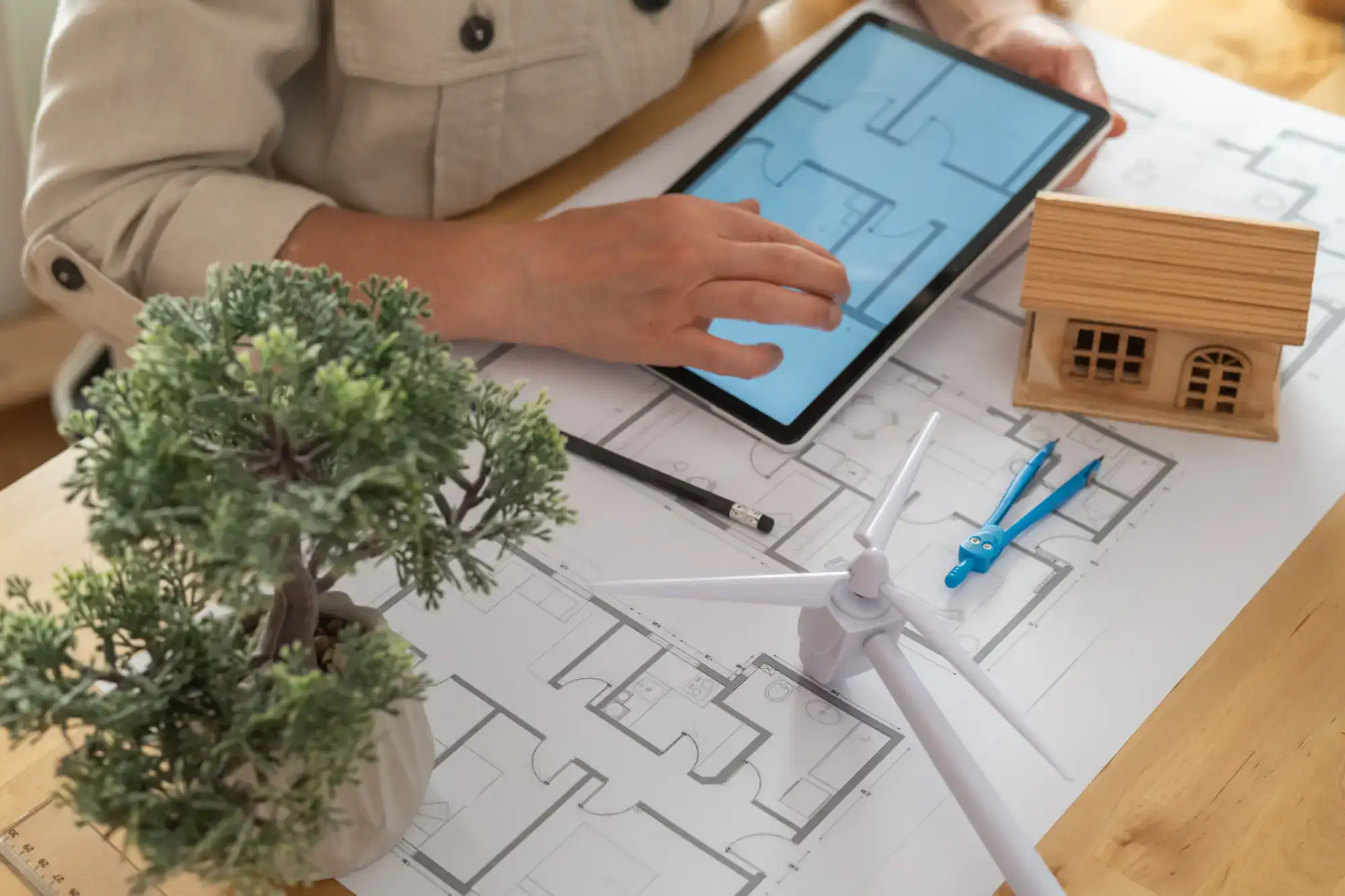 Person using a tablet to view blueprints, with a model house and wind turbine.