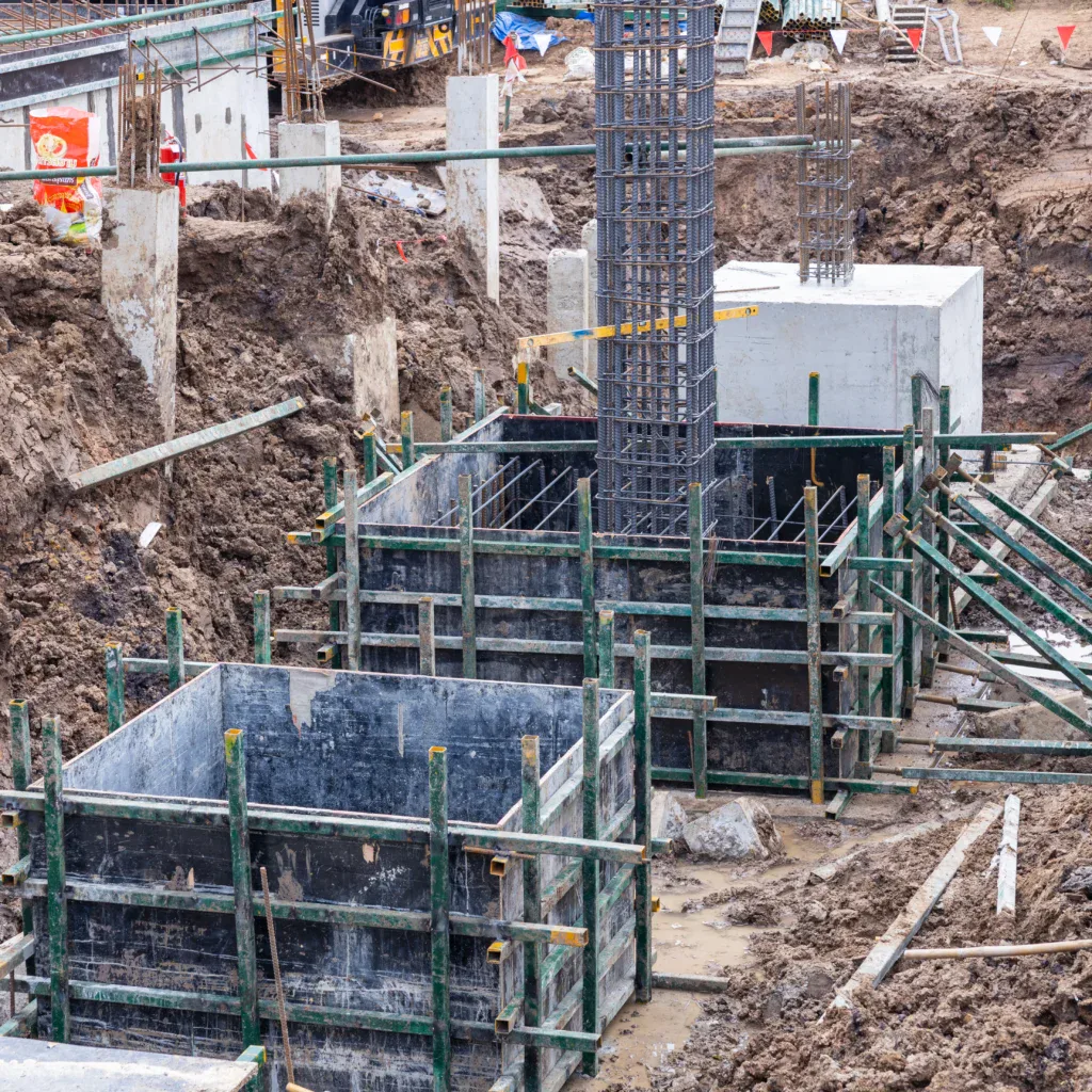 Construction site with excavated dirt, concrete foundations, and rebar structures.