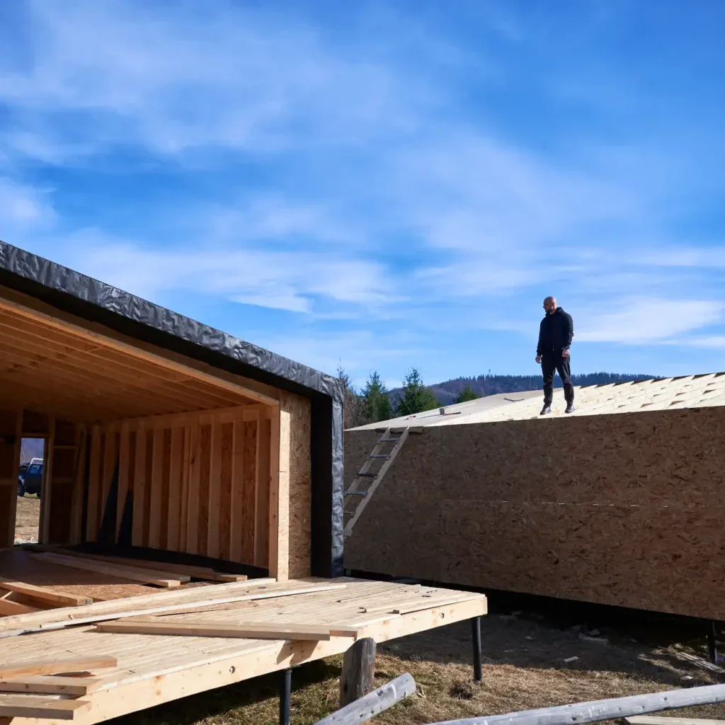 Man standing on a wooden roof of a house under construction