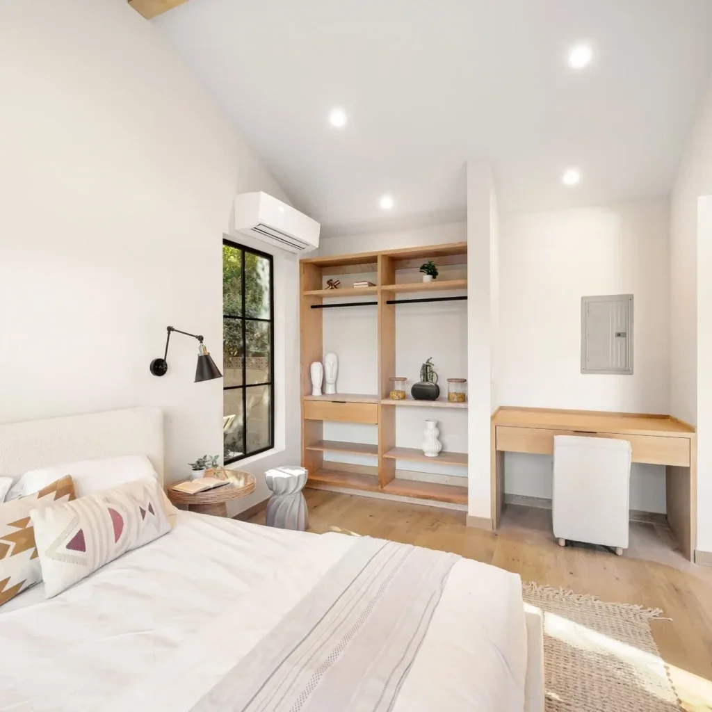Bright bedroom with white walls, a bed, open closet, and a small desk.