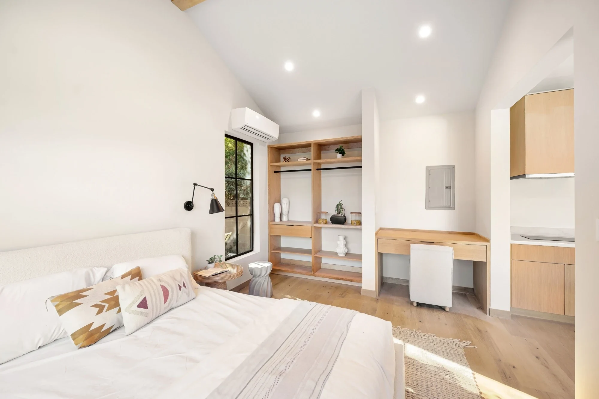 Bright bedroom with white walls, a bed, open closet, and a small desk.