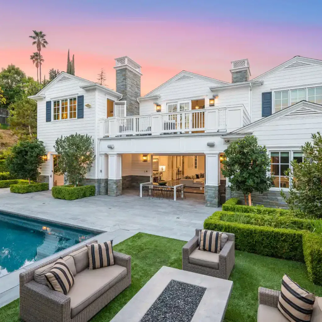 Luxury white house with pool, patio, and outdoor seating at sunset