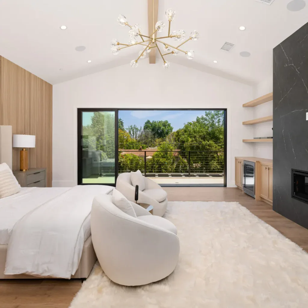 Modern bedroom with a large bed, fireplace, and view of trees.