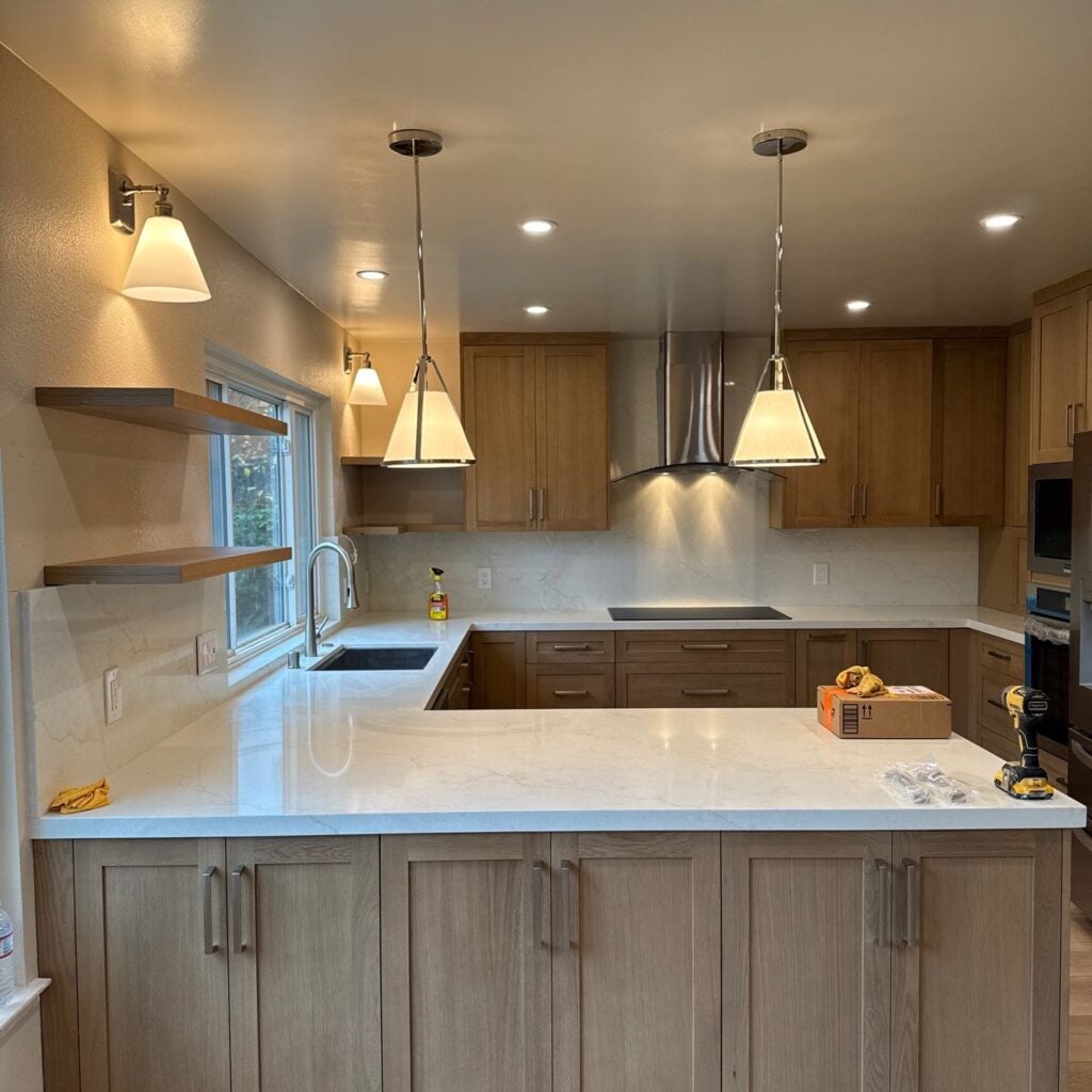 Modern kitchen with light wood cabinets, white countertops, and pendant lights.
