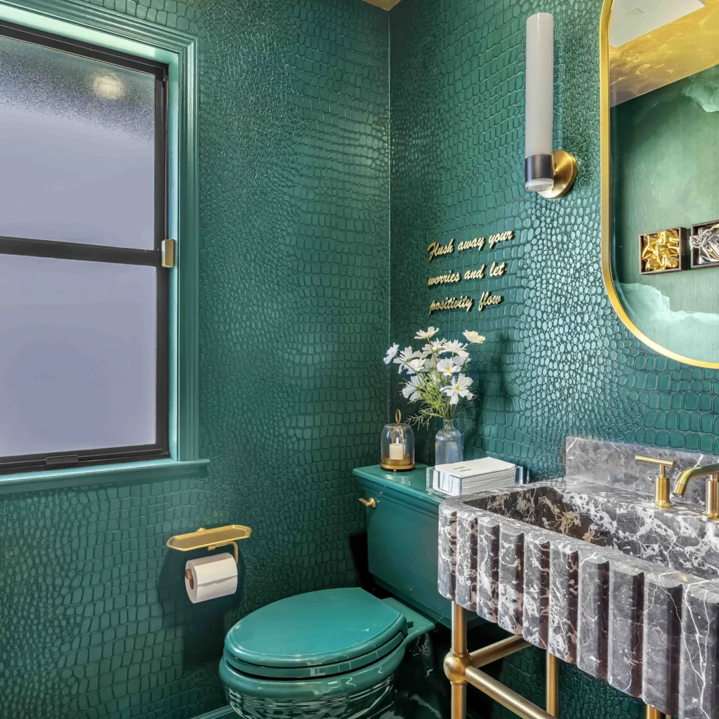 Green bathroom with a dark marble sink and a gold mirror